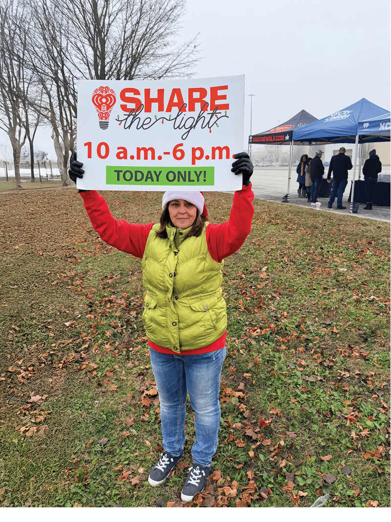 Female CU employee holding a sign advertising Share the Light Radiothon