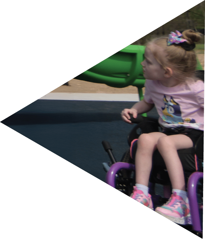 A young girl in a wheelchair is looking at a green slide.   