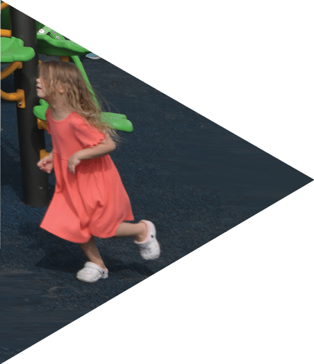 A little girl in a pink dress is running on a playground.   